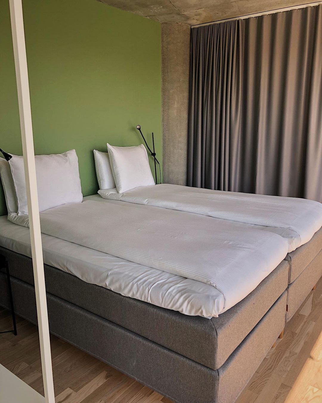 Un lit double avec du linge de lit blanc, une tête de lit grise et un mur vert.