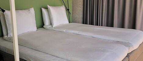 Un lit double avec du linge de lit blanc, une tête de lit grise et un mur vert.