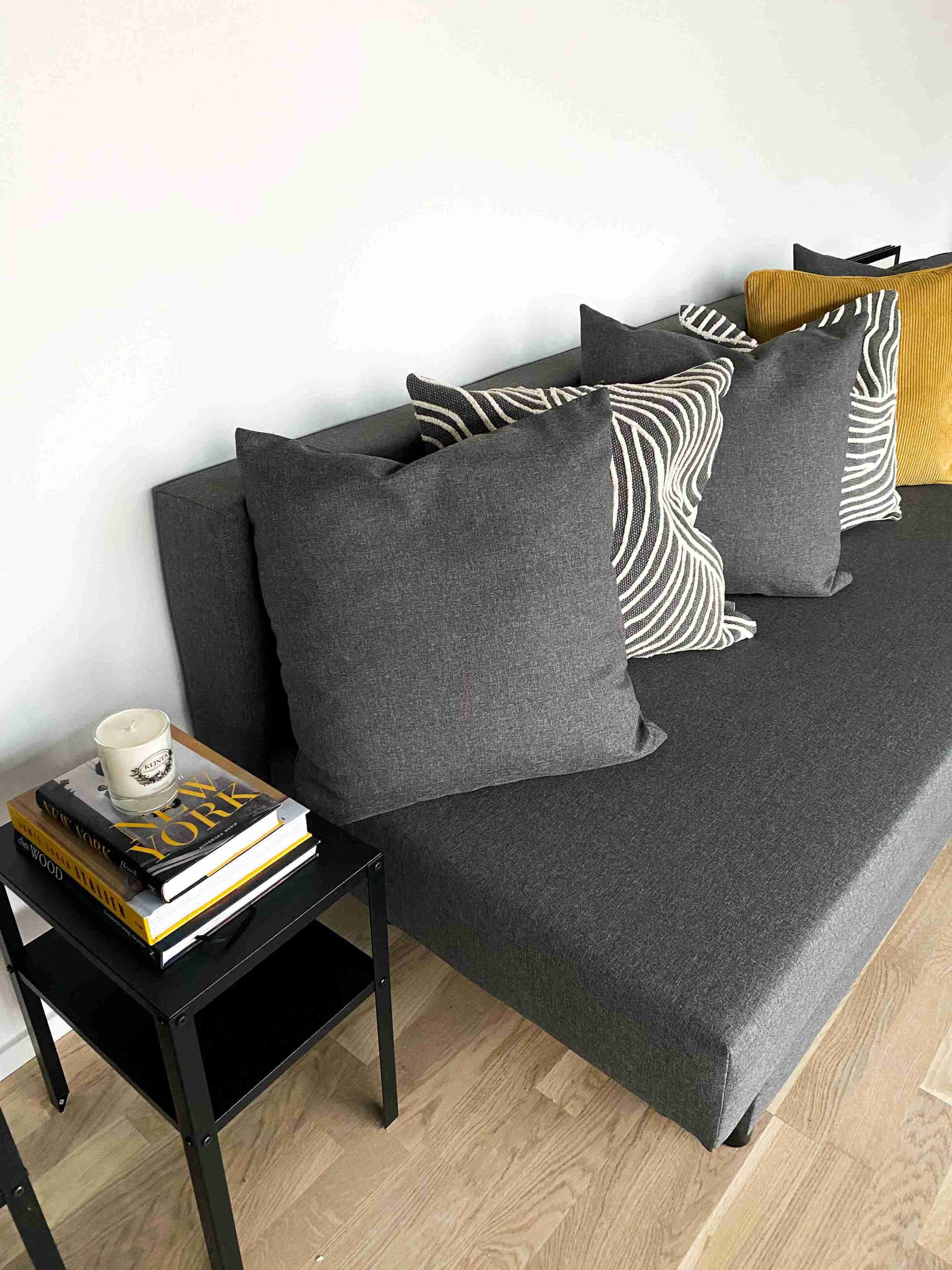 Una habitación moderna con un sofá gris, almohadones a rayas negras y blancas, y una mesita auxiliar negra con una vela blanca y libros.