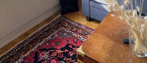 A living room with a sofa, a lamp, a vase with dried flowers, a patterned rug, and a window with curtains.