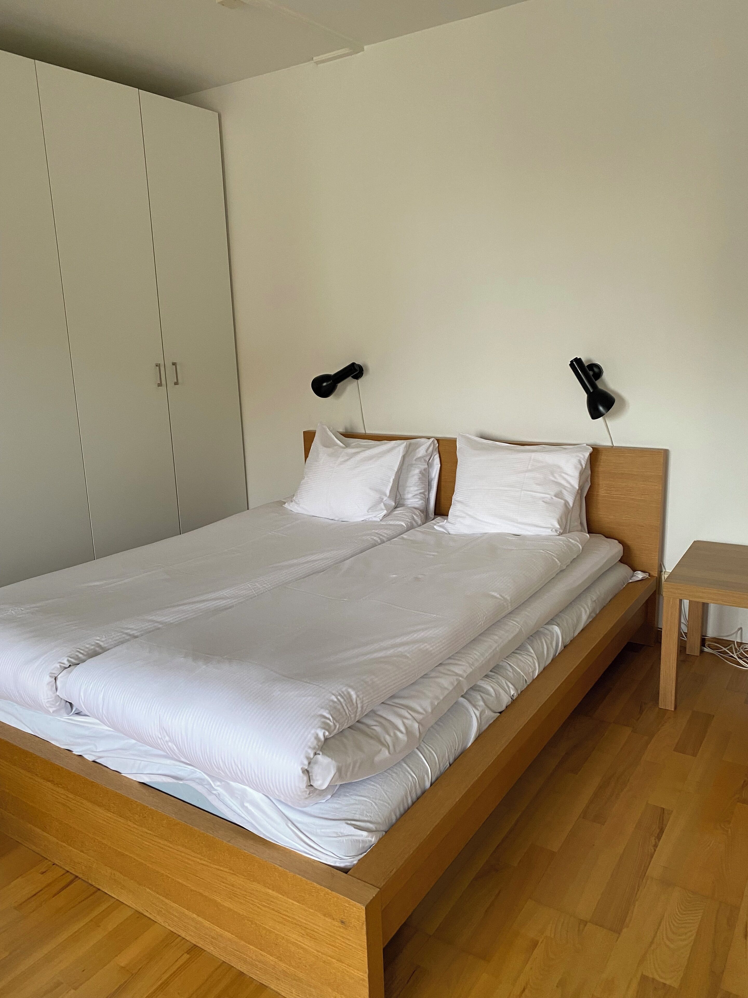 A single bed with a wooden frame and white bedding, two bedside lamps, and a wooden nightstand.