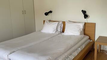 A single bed with a wooden frame and white bedding, two bedside lamps, and a wooden nightstand.