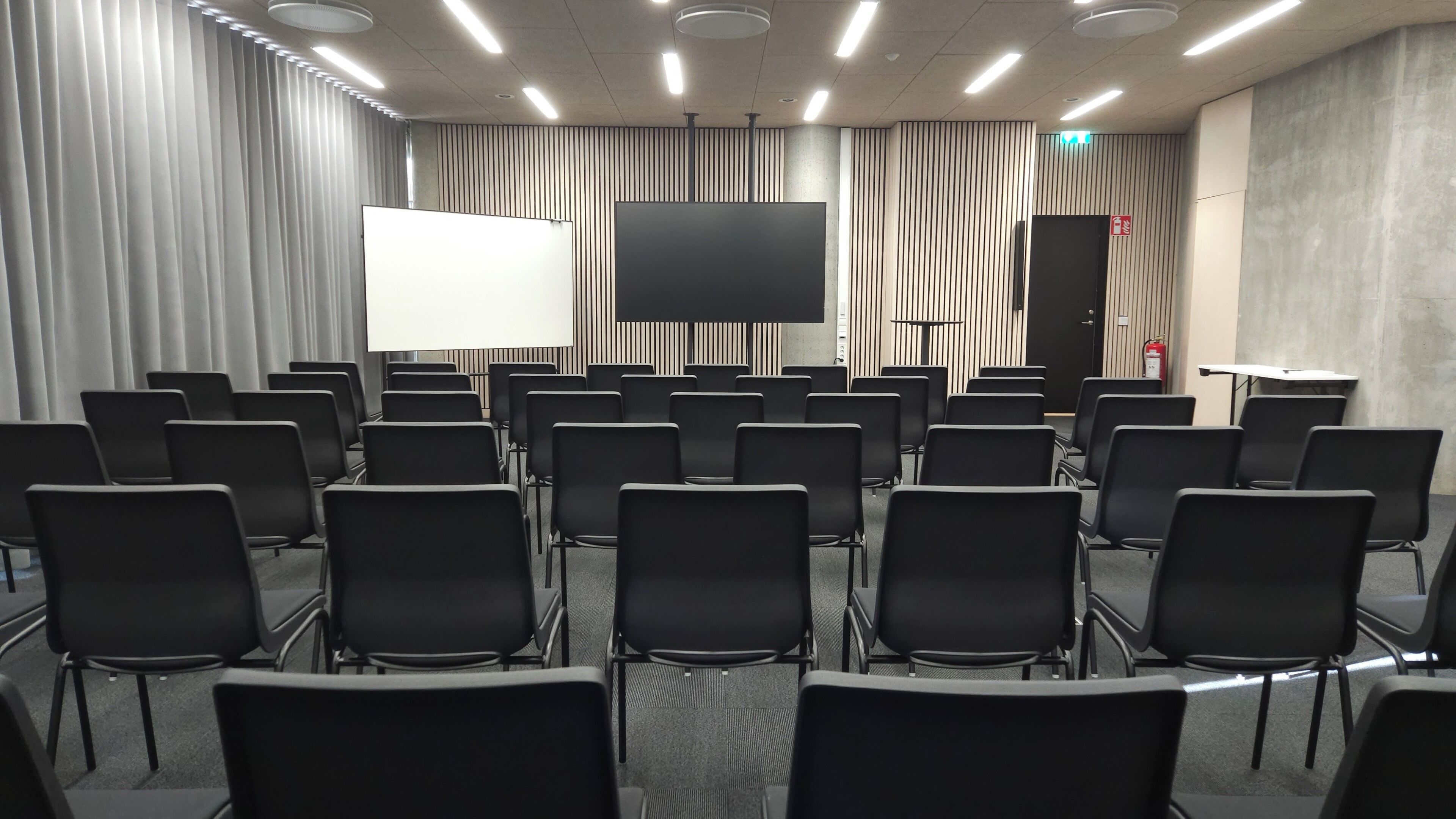 A conference room with rows of black chairs, a large white screen, and a podium.