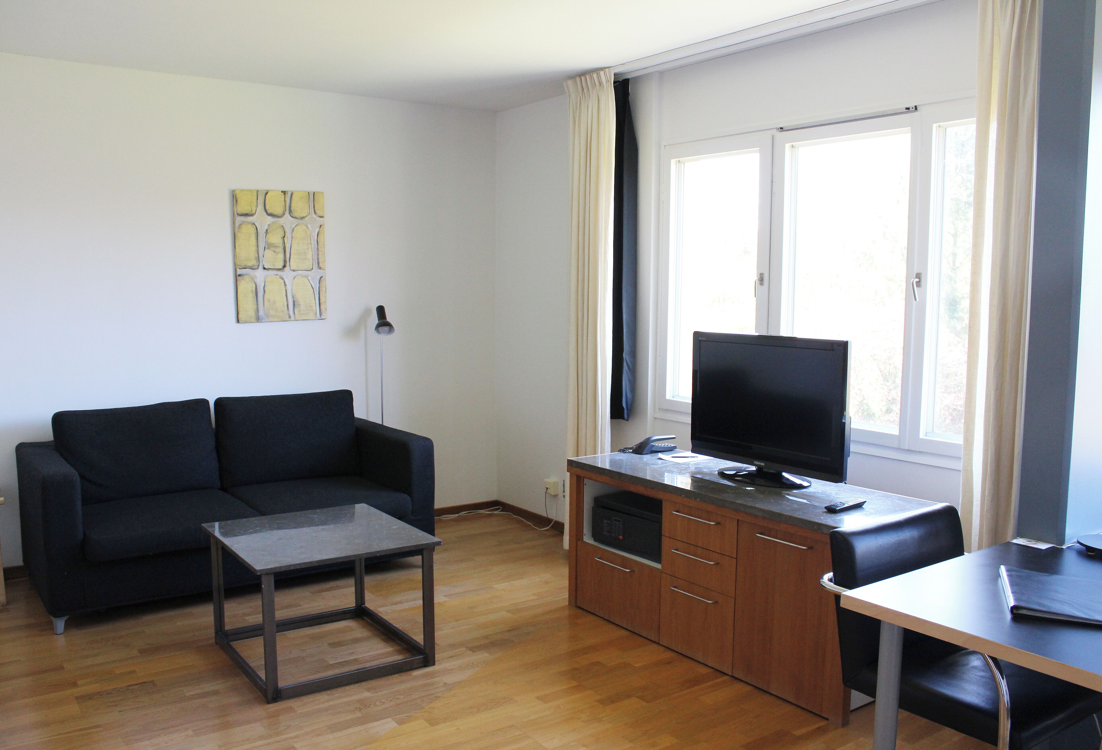 A modern living room with a black sofa, a glass-top coffee table, a wooden cabinet, and a TV on a stand.