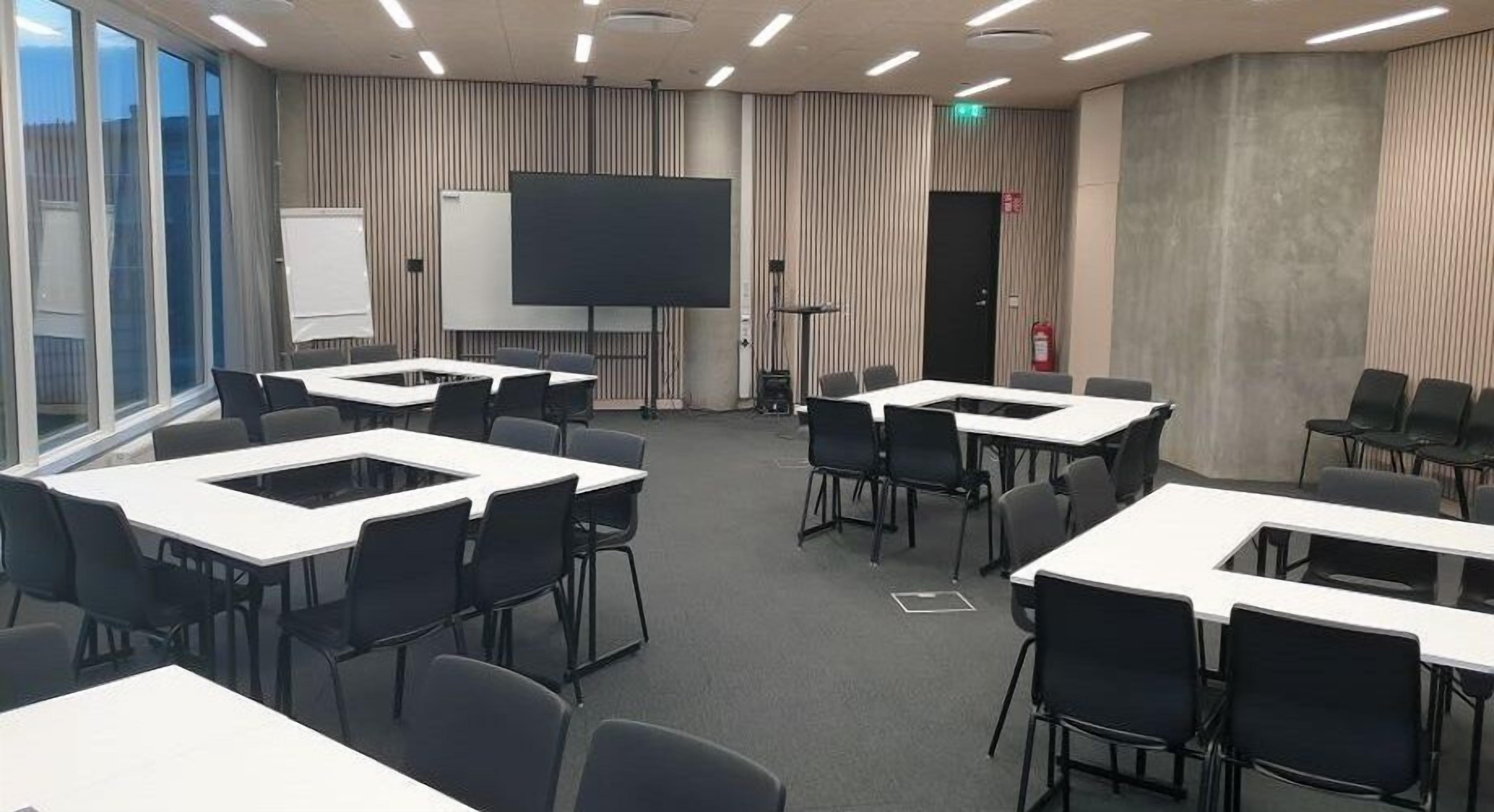 Une salle de conférence équipée de plusieurs tables et chaises, d’un grand écran et d’un tableau blanc.