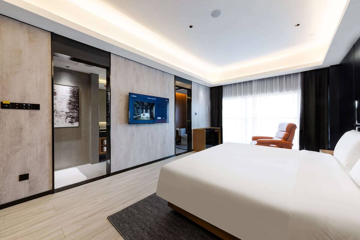 Una habitación de hotel moderna con una cama grande, un televisor de pantalla plana en la pared y un armario con puerta corredera.