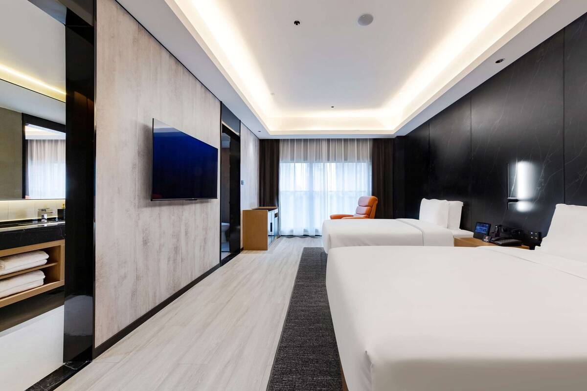 Una habitación de hotel moderna con una cama grande, televisión, escritorio y baño con espejo y toallero.
