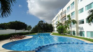 Une piscine à bord incurvé, entourée d’un bâtiment blanc doté de balcons.