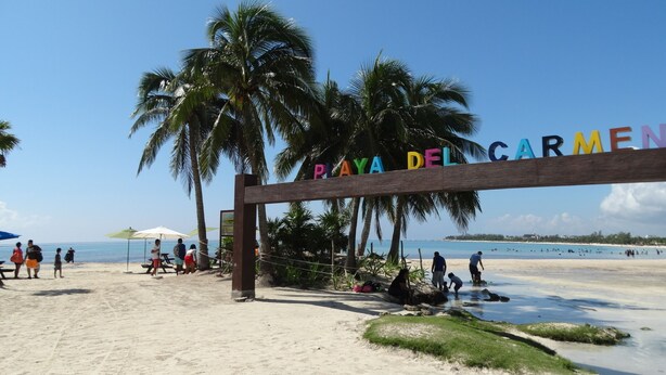 Une entrée de plage bordée de palmiers et sur laquelle on peut lire l’inscription « PLAYA DEL GARMEN ».