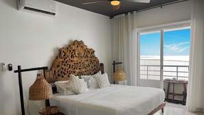 Une chambre avec un grand lit, un ventilateur de plafond, une tête de lit en bois et une vue sur le balcon.
