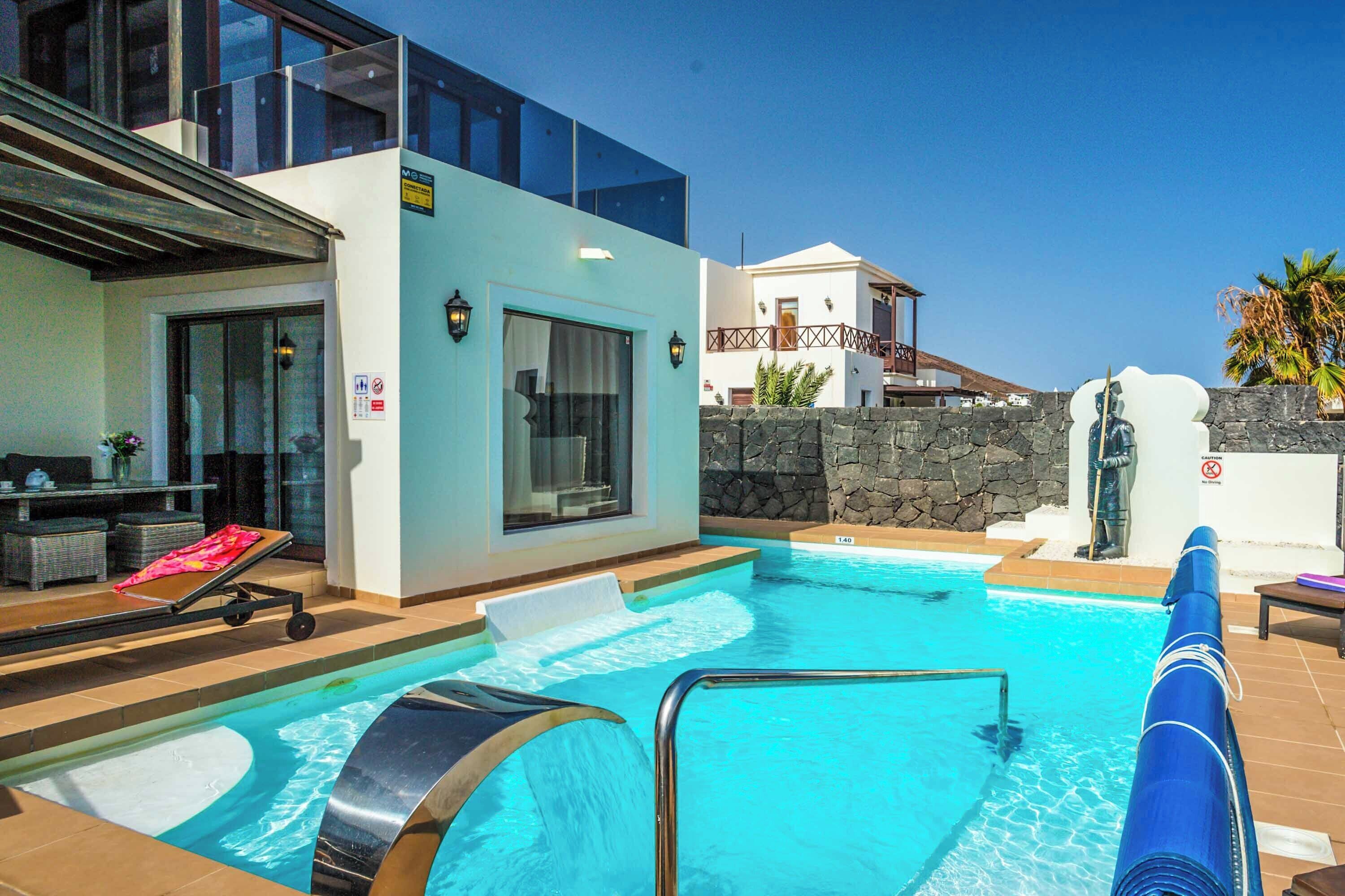 A swimming pool with a water slide, lounge chairs, and a stone wall.