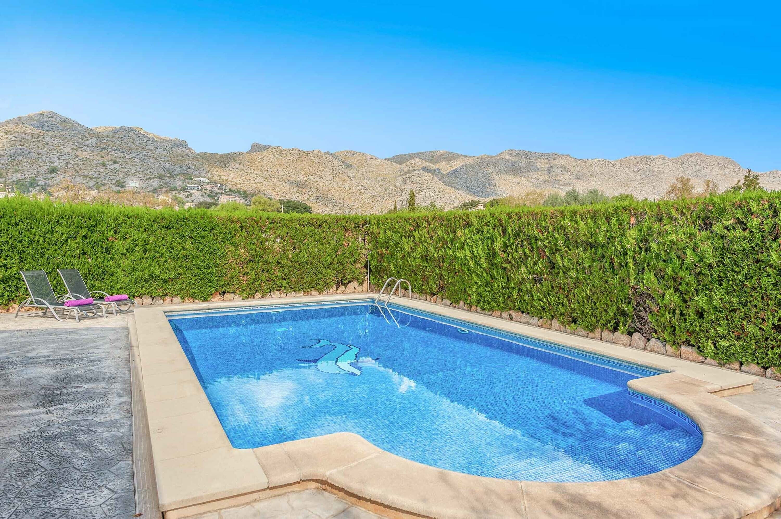 Una piscina de borde curvo, rodeada por un seto bajo y con vistas a montañas al fondo.
