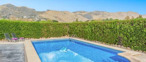 Una piscina de borde curvo, rodeada por un seto bajo y con vistas a montañas al fondo.