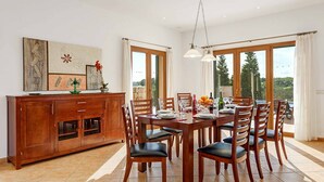 Un comedor con una mesa de madera dispuesta para seis personas, rodeada de sillas. A la izquierda, un armario de madera con puertas de cristal.