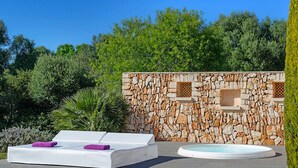 Pared de piedra con bañera de hidromasaje integrada y zona de descanso blanca con toallas moradas.
