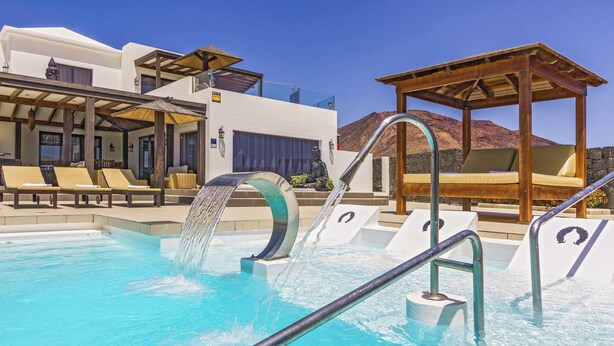 A swimming pool with a waterfall feature, lounge chairs, and a wooden pergola.