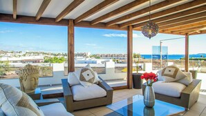 A modern outdoor seating area with a view of the sea and buildings.