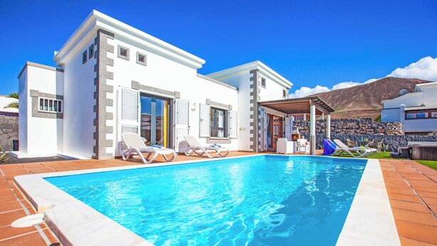 Une maison moderne dotée d’une piscine, de chaises longues et d’une pergola.
