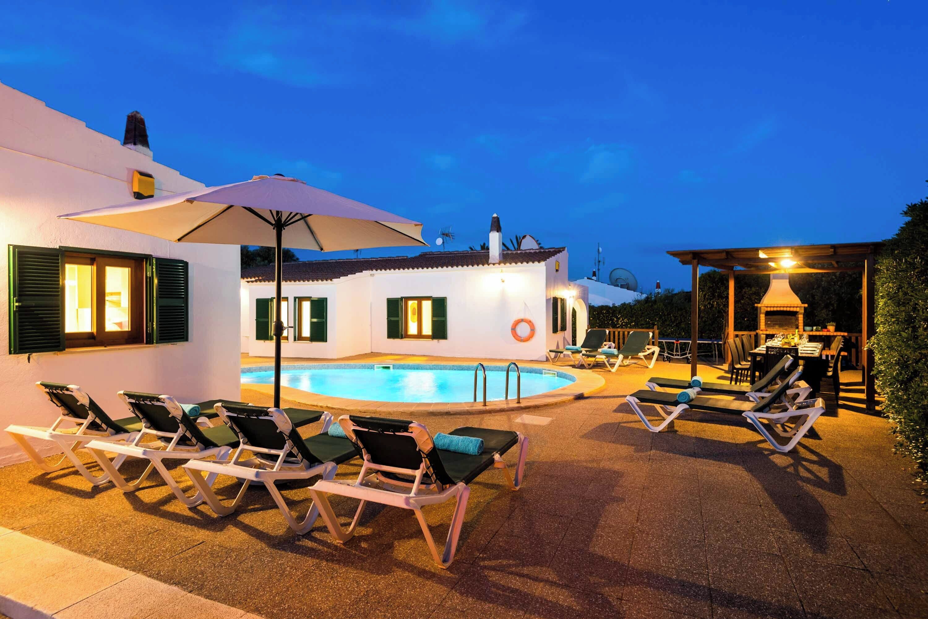 Zona de piscina con sillones de descanso y sombrillas, una piscina y un área de comedor con mesas y sillas.