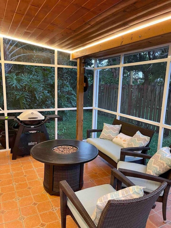 A covered patio area with a round table, wicker furniture, and a grill.