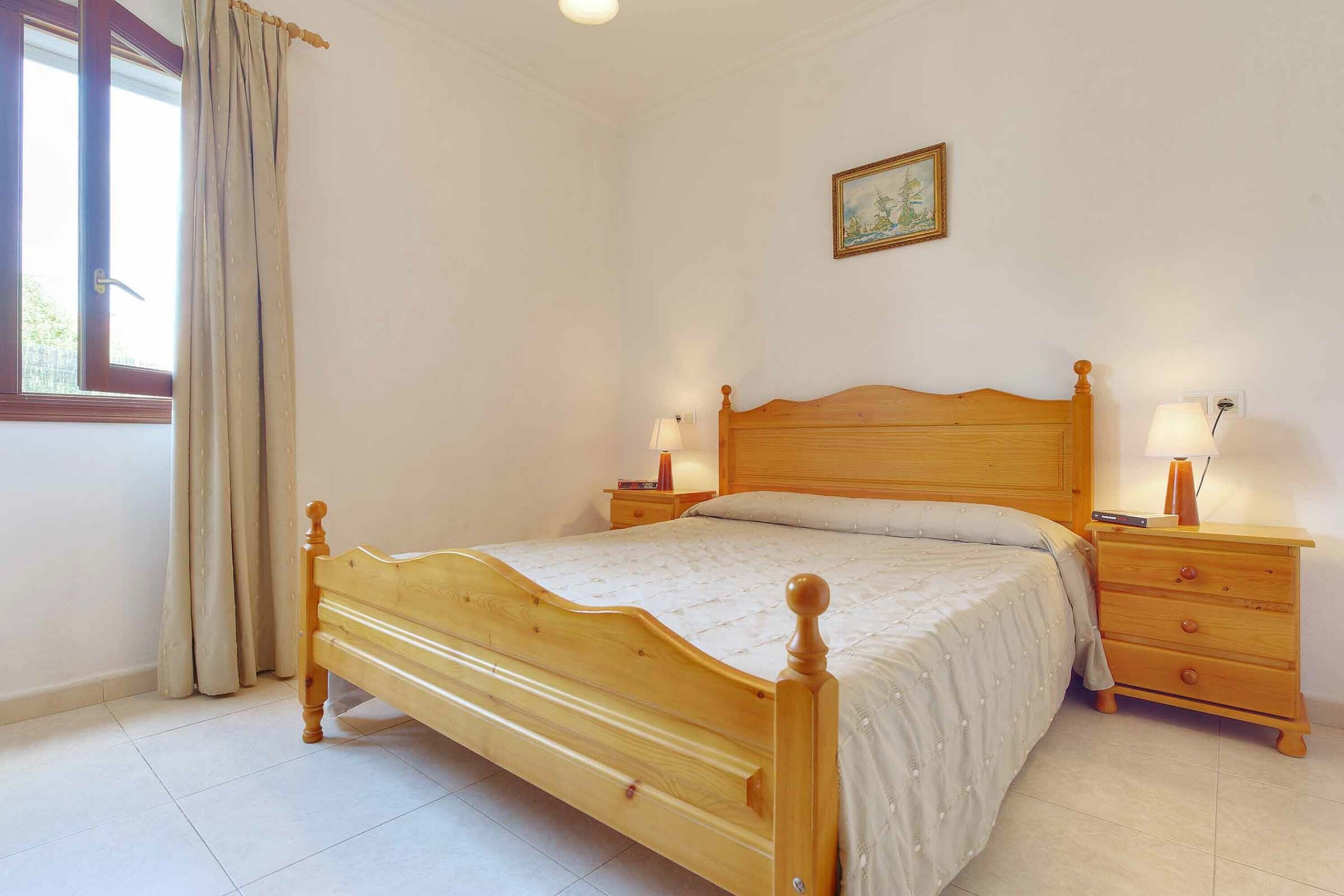 Une chambre à coucher avec un lit en bois, des tables de chevet avec des lampes, une fenêtre avec des rideaux et un tableau au mur.