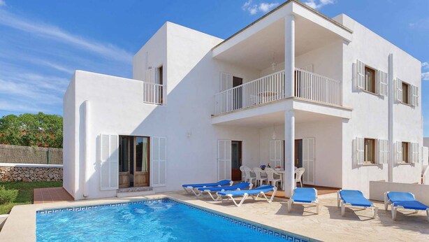 A modern two-story building with a swimming pool, outdoor seating, and a stone wall. - Villa La Pinta - Five Bedroom Villa, Sleeps 10 (Cala d'Or)