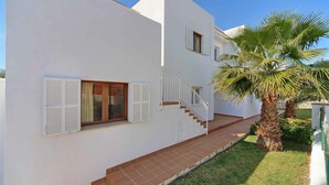 A modern two-story house with white exterior walls, a wooden door, and a staircase leading to the upper floor. - Villa La Pinta - Five Bedroom Villa, Sleeps 10 (Cala d'Or)
