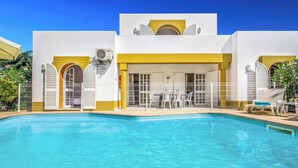 Ein Poolbereich mit klarem, blauem Pool, einem weiß-gelben Gebäude und Gartenmöbeln.
