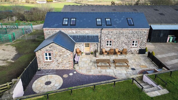 A stone building with a sloped roof, a patio with wooden furniture, and a view of the countryside.