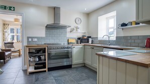A modern kitchen with a built-in oven, microwave, and sink. There is a clock on the wall and a window providing natural light.