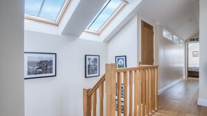 A hallway with skylights, wooden railings, and framed pictures on the walls.
