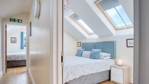 A bedroom with a skylight, a bed with a blue headboard, a bedside table, and a nightstand.