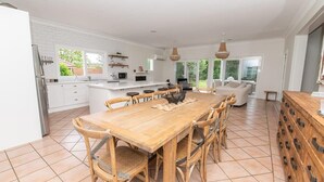 Een ruime keuken met een grote houten eettafel, witte kasten en uitzicht op de tuin.