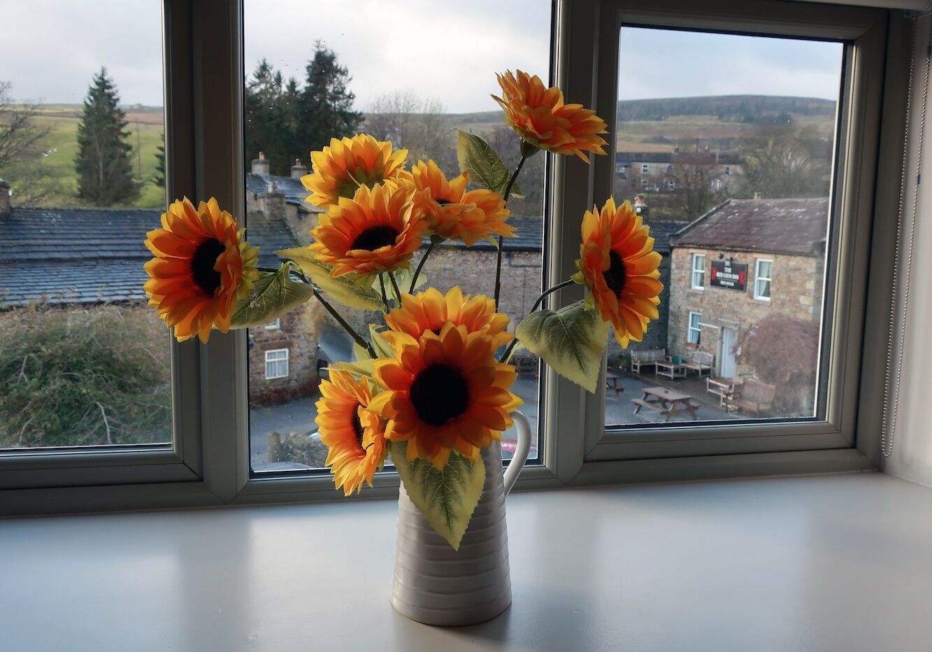 Un jarrón con girasoles en un alféizar.