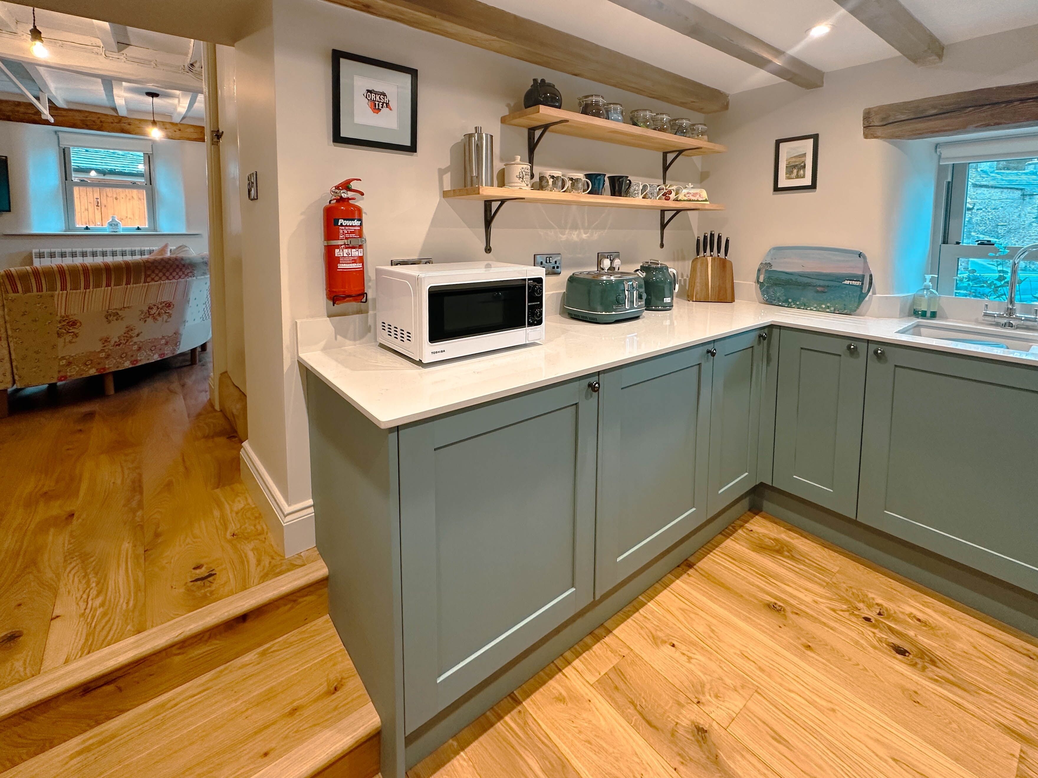 Cocina con gabinetes grises, un microondas blanco y estantes de madera arriba.