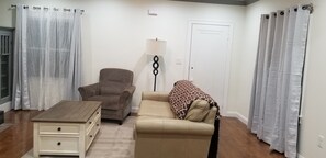 A living room with a brown armchair, a beige sofa, a wooden coffee table, and a floor lamp.