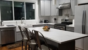 A modern kitchen with grey cabinets, a central island with bar stools, a built-in oven, and a window overlooking the room. - Newly Renovated Open-Concept living space, close to Boston, plenty of parking (Milton)