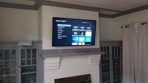 A flat-screen TV mounted above a white brick fireplace with a remote control on the left. - Newly Renovated Open-Concept living space, close to Boston, plenty of parking (Milton)