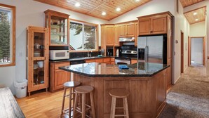 Une cuisine moderne avec des meubles en bois, un plan de travail en granit, des appareils électroménagers en acier inoxydable et un grand îlot central doté de tabourets de bar.