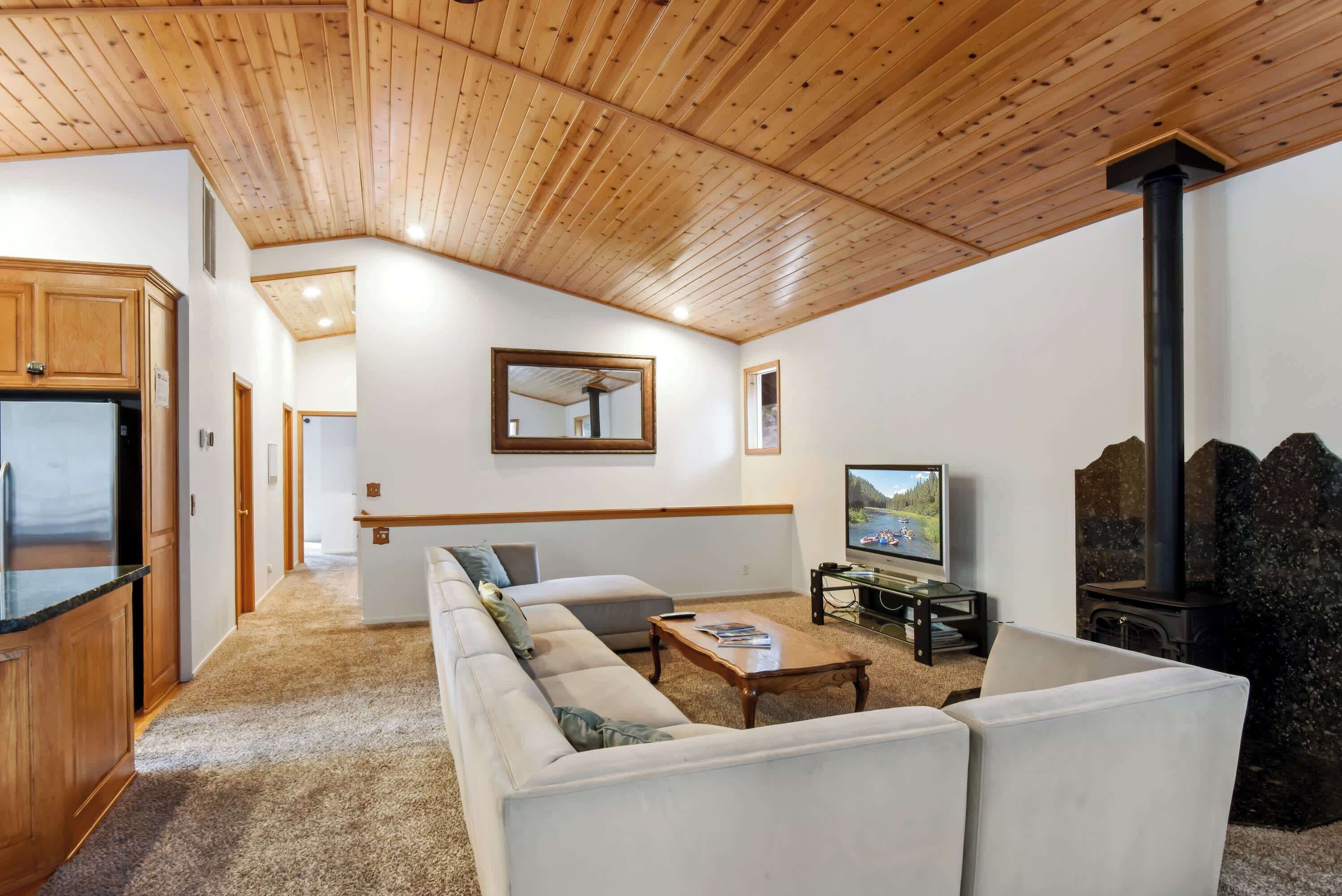 A living room with a sofa, coffee table, TV, fireplace, and wooden ceiling.