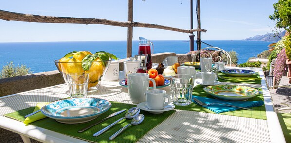 An outdoor dining setup with a table set for breakfast, overlooking the sea.