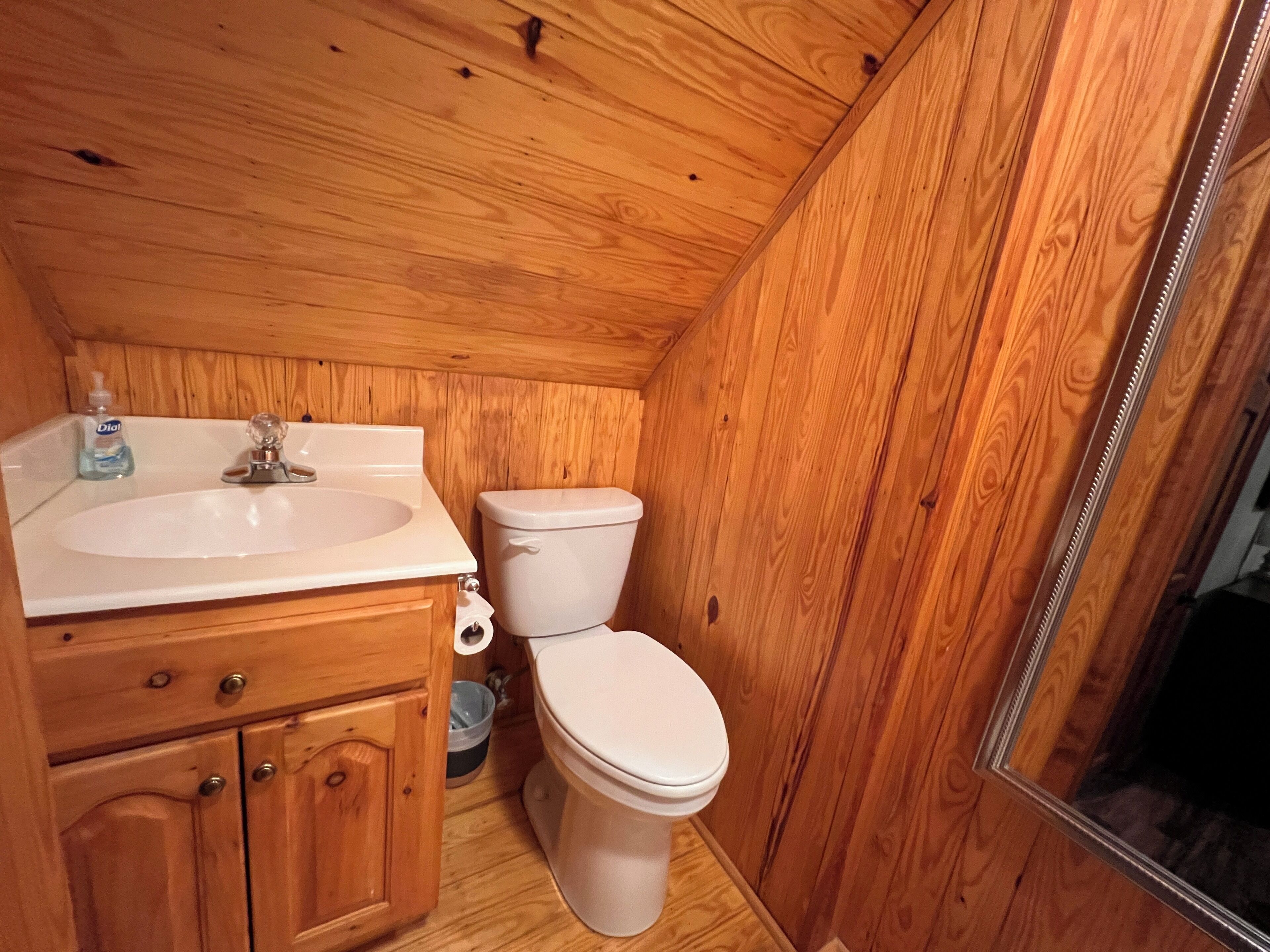 A small, wooden-paneled bathroom with a sink, toilet, and cabinet.