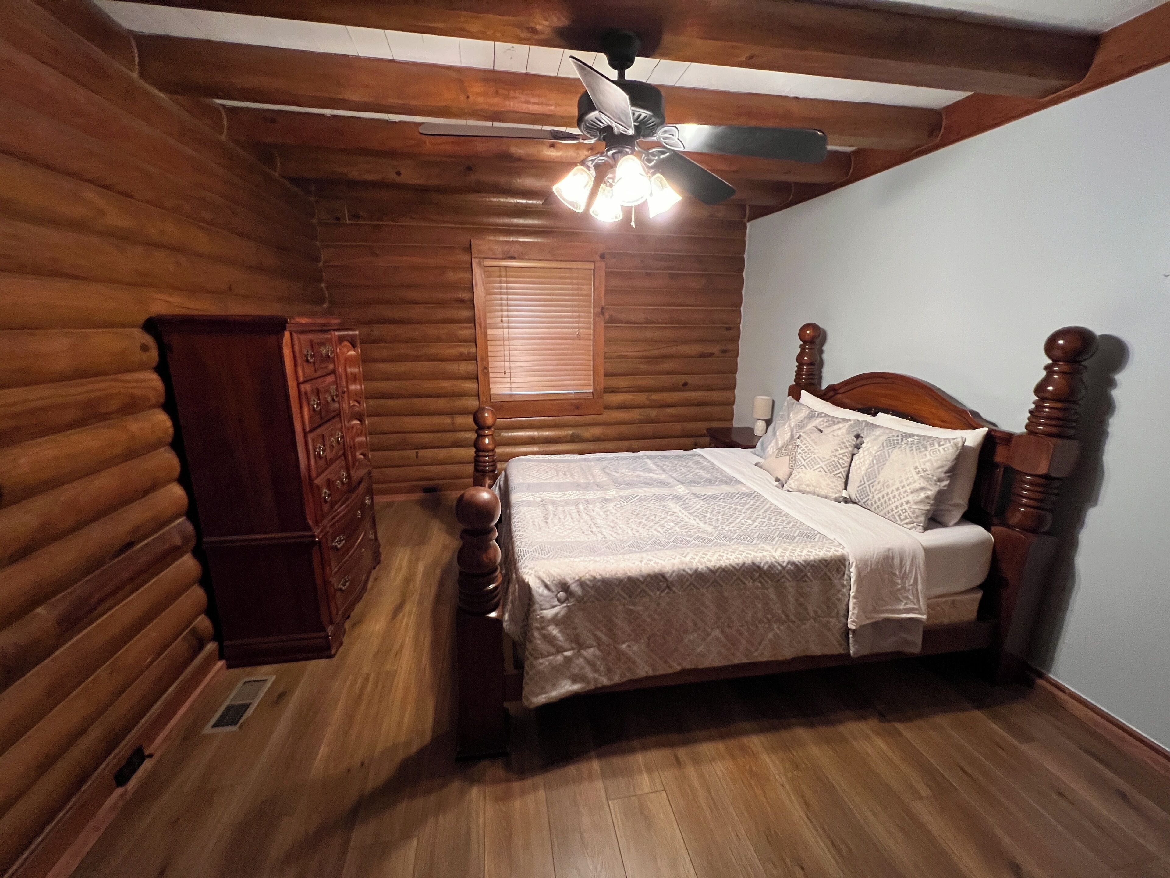 A log cabin bedroom with a wooden bed, dresser, and a ceiling fan.