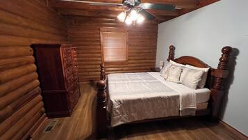 A log cabin bedroom with a wooden bed, dresser, and a ceiling fan.