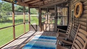 Eine Holzterrasse mit einem blauen, gemusterten Teppich, Holzstühlen und einem Rettungsring an der Wand.
