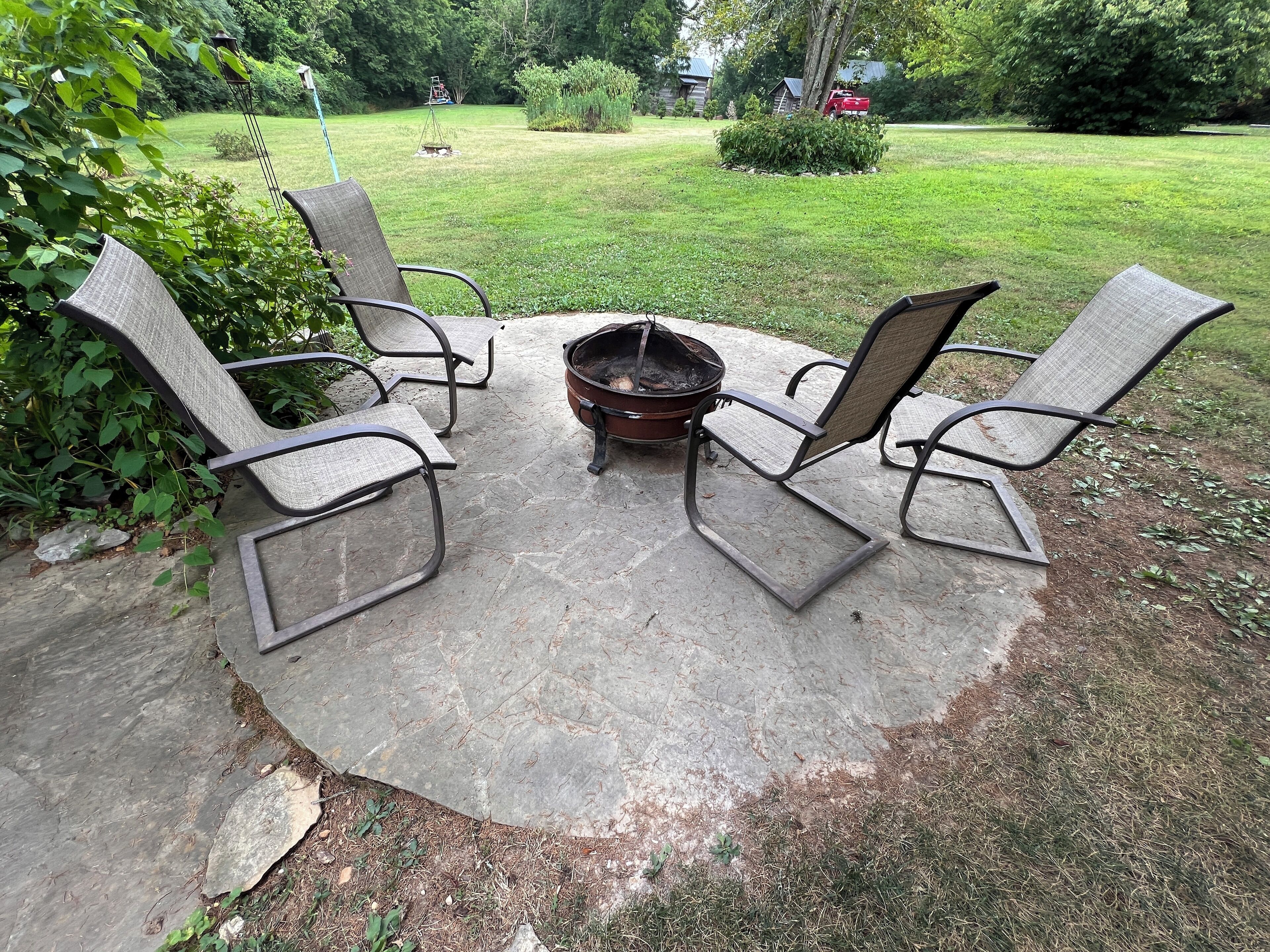 A concrete patio with four metal chairs and a central fire pit.