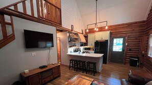 Ein gemütliches Blockhaus-Interieur mit einer Holztreppe, einem Essbereich mit Tisch und Stühlen, einer Küche mit Kochinsel und einem Wohnzimmer mit Sofa.