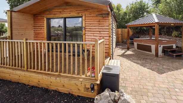 A wooden cabin with a balcony, a hot tub, and a covered seating area. - Celyn (Ruthin)