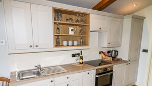 A modern kitchen with white cabinetry, a wooden countertop, a built-in wine rack, and a coffee maker. - Celyn (Ruthin)