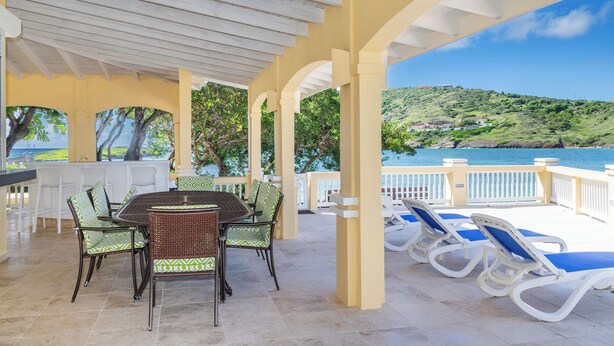 A covered outdoor area with a dining table and chairs, a poolside lounge area, and a view of a hillside and water. - Wake up in paradise at this amazing villa for couples and families (St.Paul)